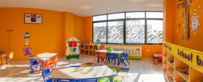 Turuncu anaokulu sınıfında yuvarlak masalar ve oyun köşesi