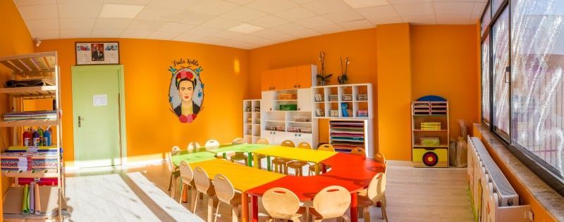 Renkli küçük masaları ve sandalyeleri olan turuncu anaokulu sınıfı