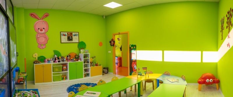 Oyuncak dolabı ve küçük masaları olan yeşil anaokulu sınıfı